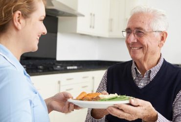 Carer Serving Lunch To Senior Man