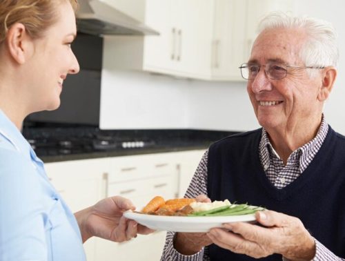 Carer Serving Lunch To Senior Man
